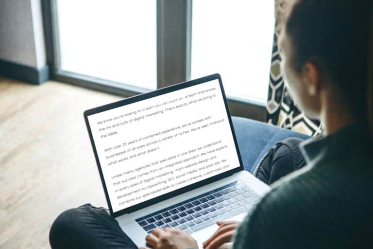 Person sitting on a couch writing copy on a laptop.